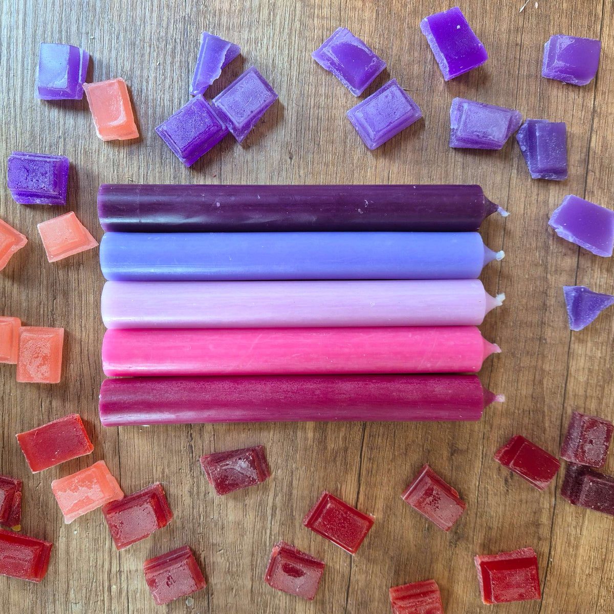 Fünf Stabkerzen in Violett, Flieder, Rosa, Pink und Bordeaux liegend auf Holz