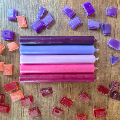 Fünf Stabkerzen in Violett, Flieder, Rosa, Pink und Bordeaux liegend auf Holz