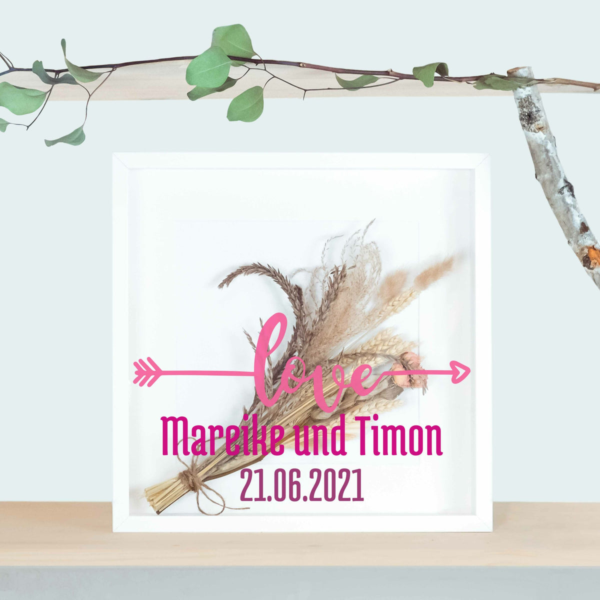 Weißer Brautstraußrahmen mit „love“-Schriftzug und Pfeil, Namen und Datum in Pink über Trockenblumen