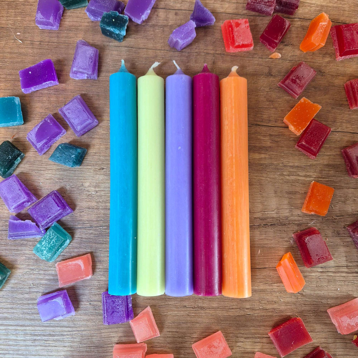 Fünf Stabkerzen Flower Power liegend auf Holz zwischen bunten Wachswürfeln