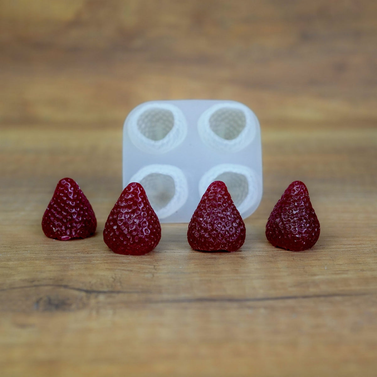 Quadratische Silikonform mit 4 Beeren-Mulden und vier dunkelrot gegossenen Wachserdbeeren