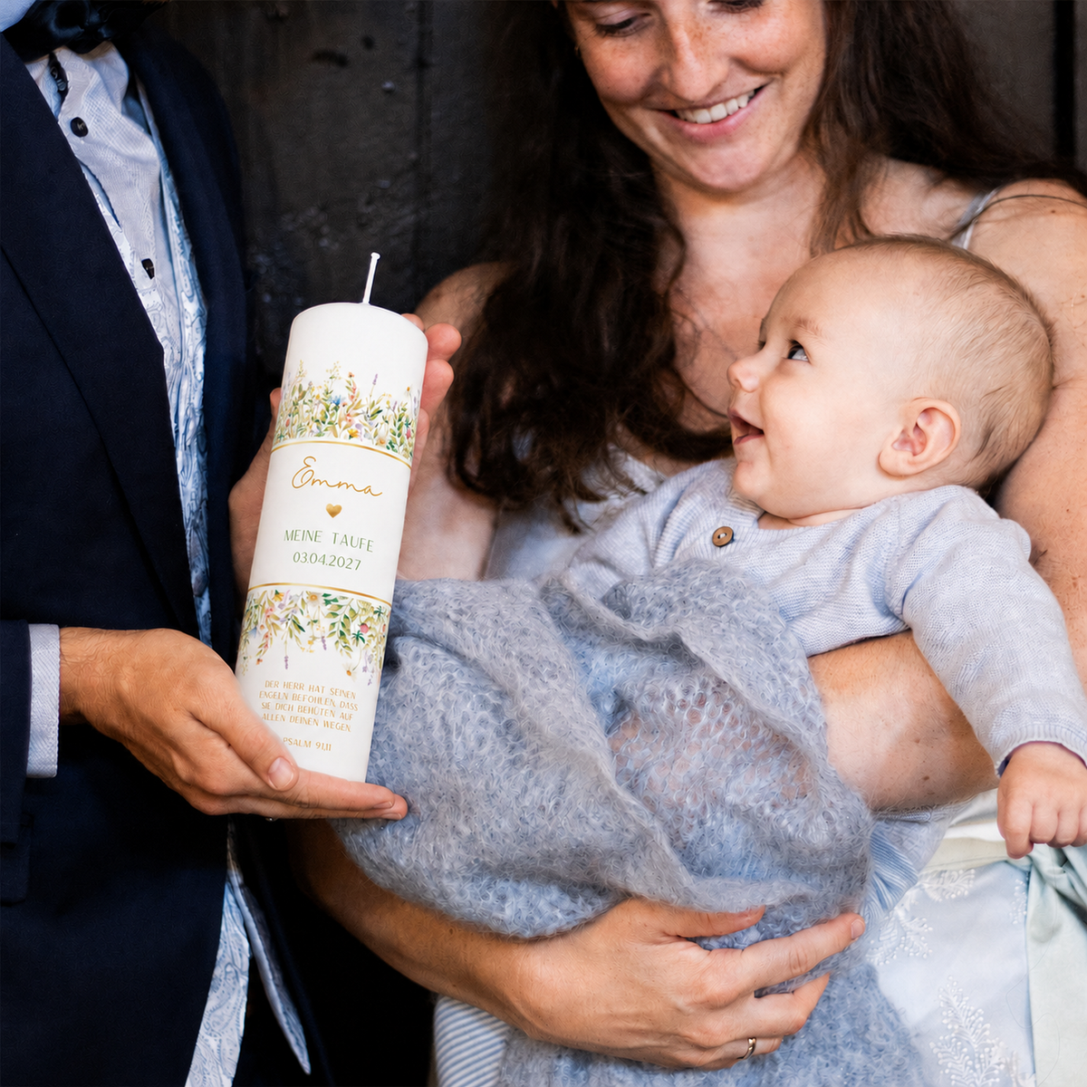 Eltern halten Baby und die personalisierte Taufkerze Wiesenblumen bei der Taufzeremonie